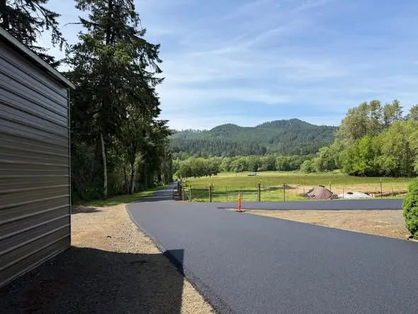 New asphalt drive beside a metal shop building, hills in the distance